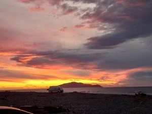 Sunset view of a beach with a campervan in the distance and an island beyond that